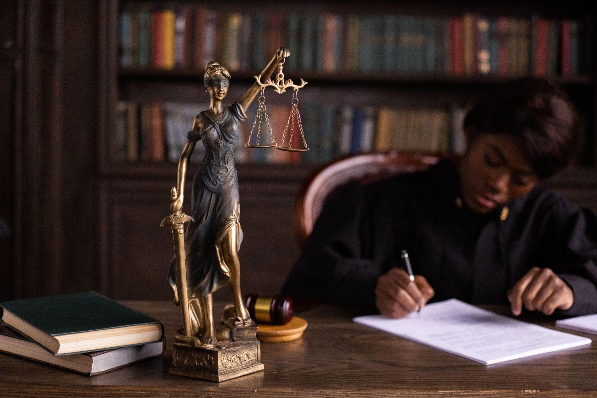 A statue of Lady Justice and a gavel on a desk while a legal professional writes notes